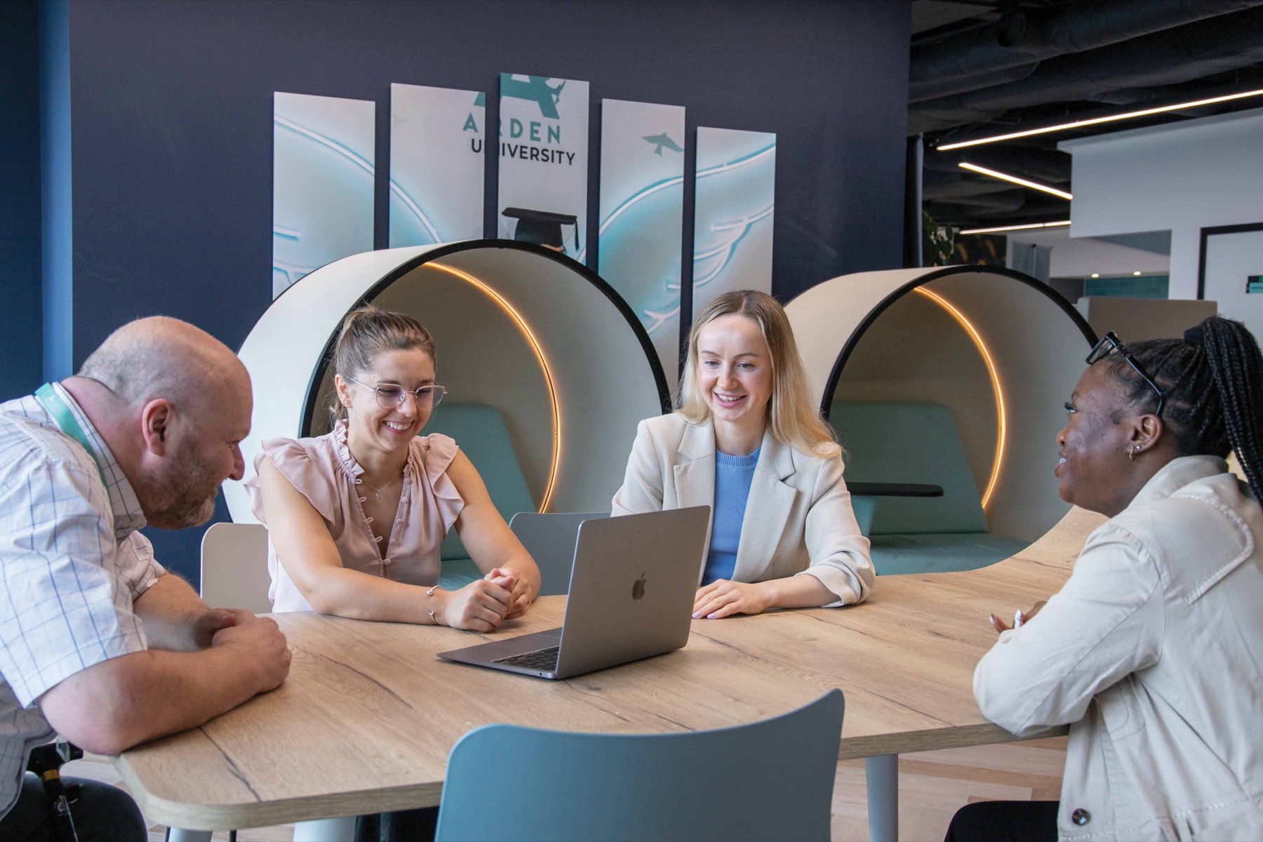 Four Arden students talking around a laptop in a study centre
