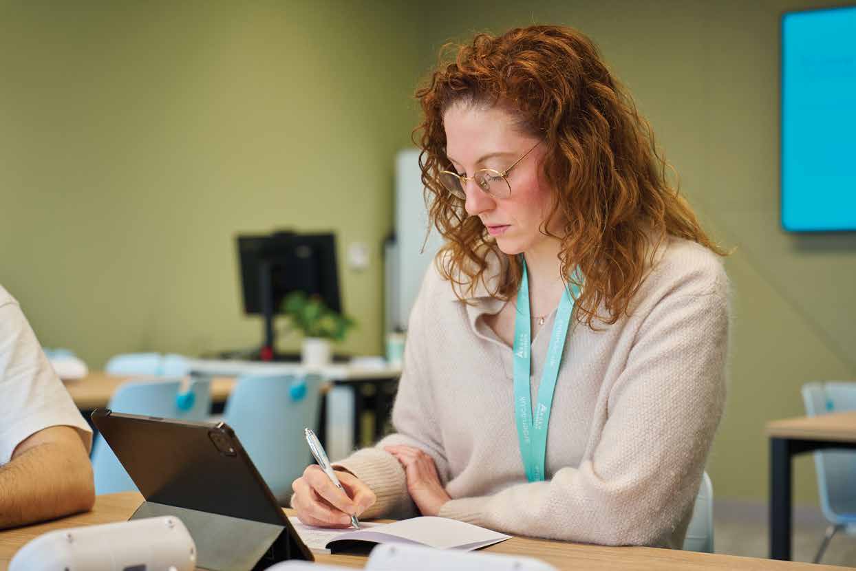 An Arden student making notes beside a tablet