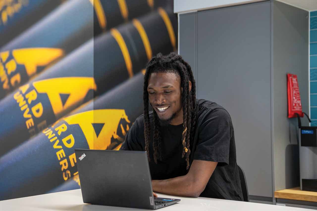 An Arden student smiling as he works on a laptop