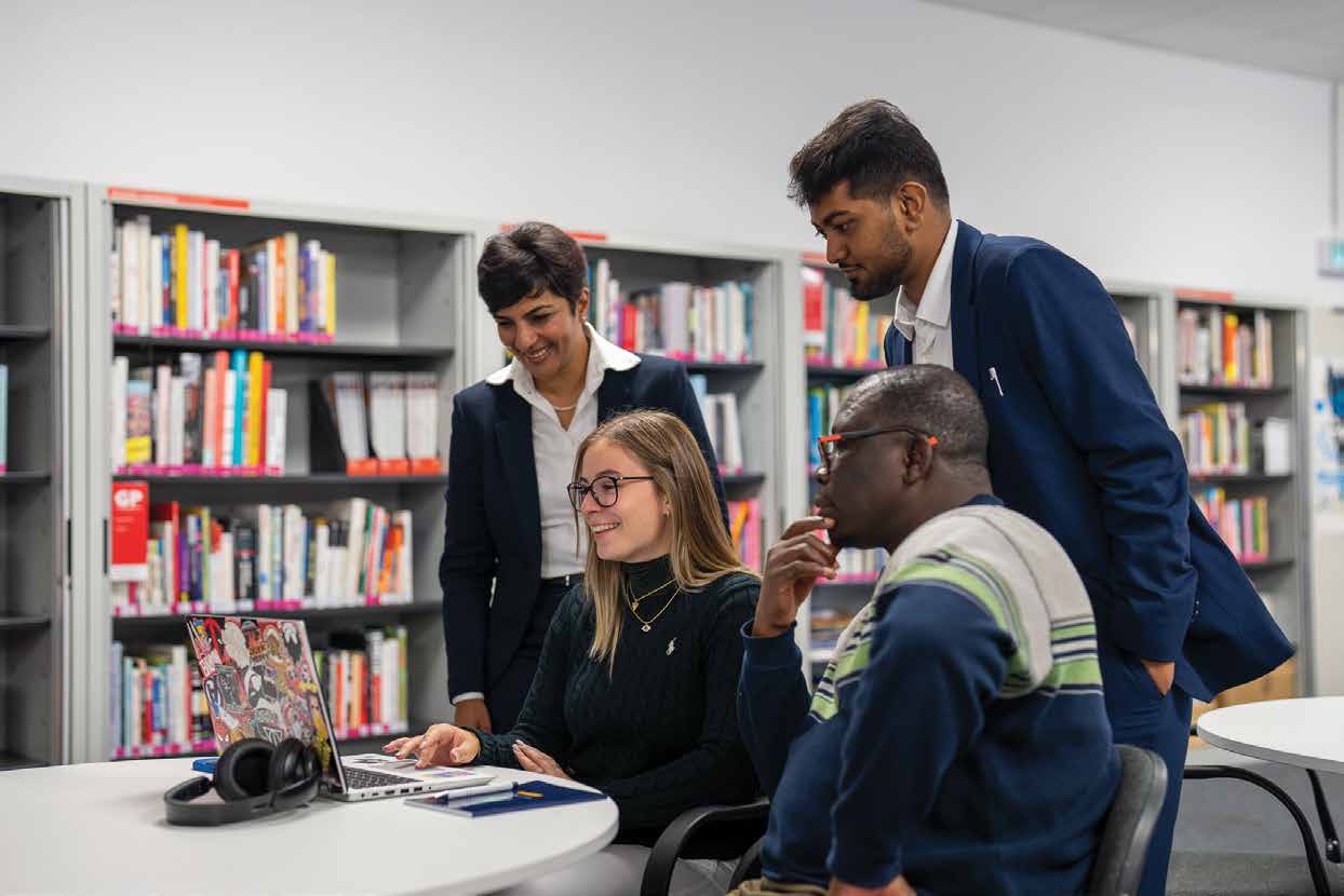 Arden students and a tutor talking around a laptop in a library